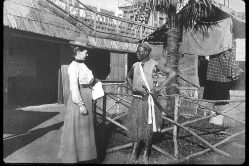 A man wearing traditional African attire, talking to a woman with early 1900s attire.