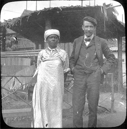A woman wearing traditional African attire, with a man wearing an early 1900s suit.