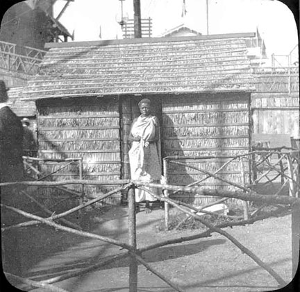 A woman standing at the doorway of a small hut.