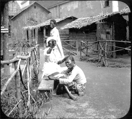 Three people near wooden fences and straw houses.
