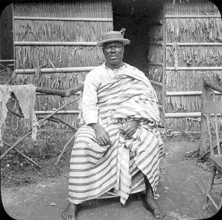 A man sitting with a hat and striped attire.